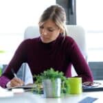 Woman writing notes during zoom meeting at desk