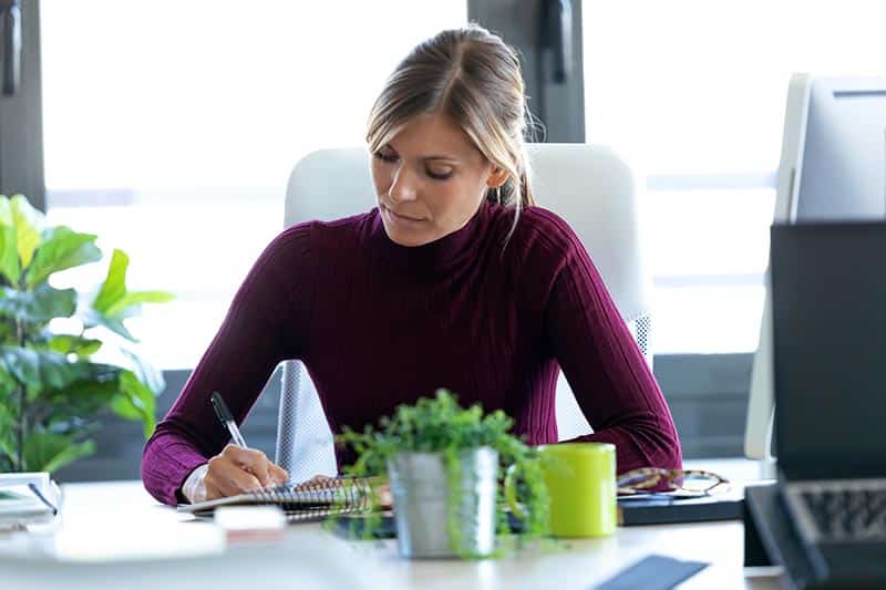 Woman writing notes during zoom meeting at desk